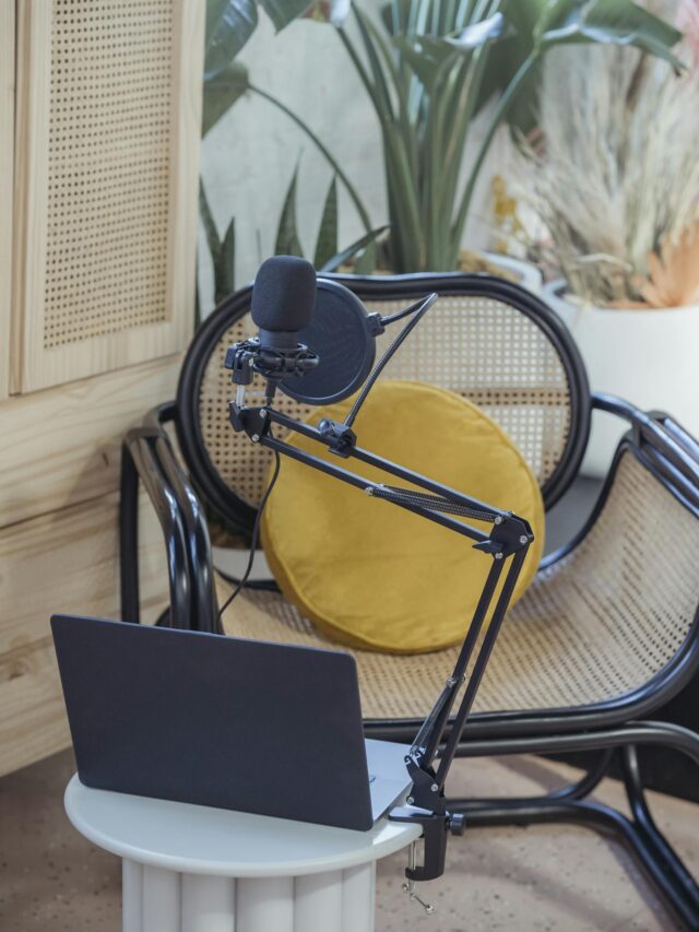 Modern laptop and microphone on tripod placed near wicker chair in modern studio before recording podcast